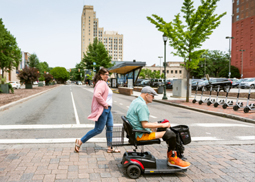 Elderly man on a scooter crossing the street.