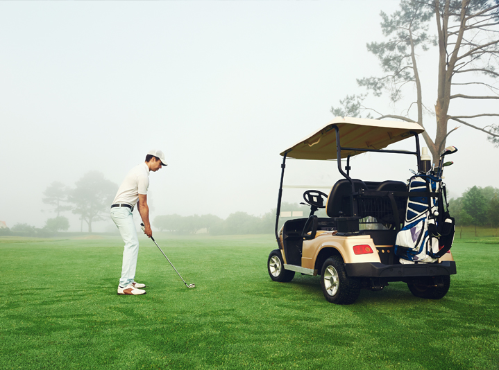 Man golfing on a course next to his golf cart.