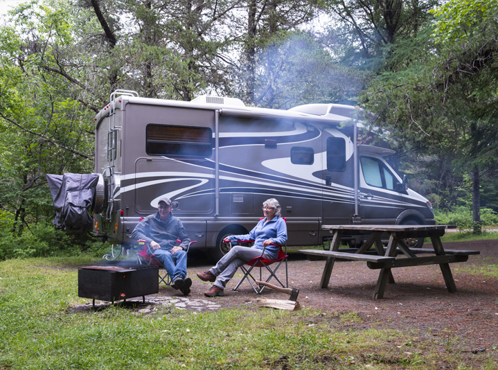 Couple sitting by a campfire and their RV camping.